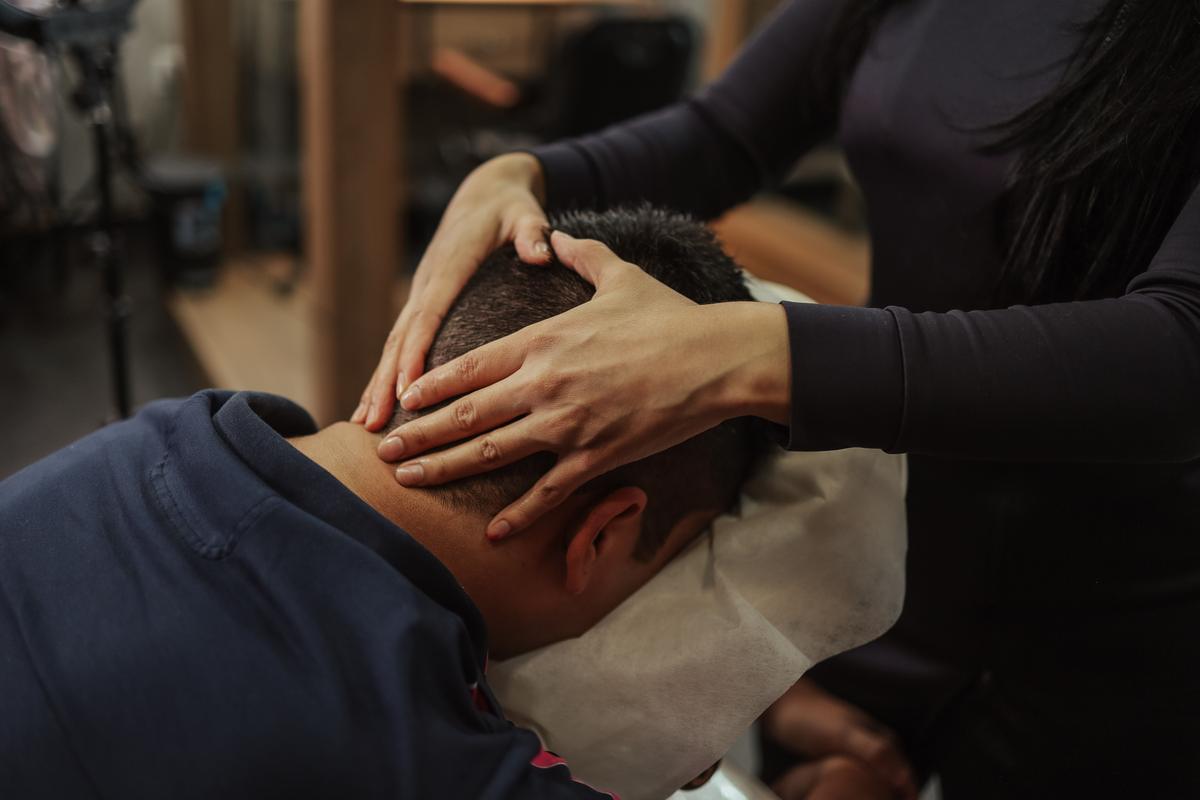 A staff member's hands massaging the head of a seated client at a salon, his face turned away from the camera