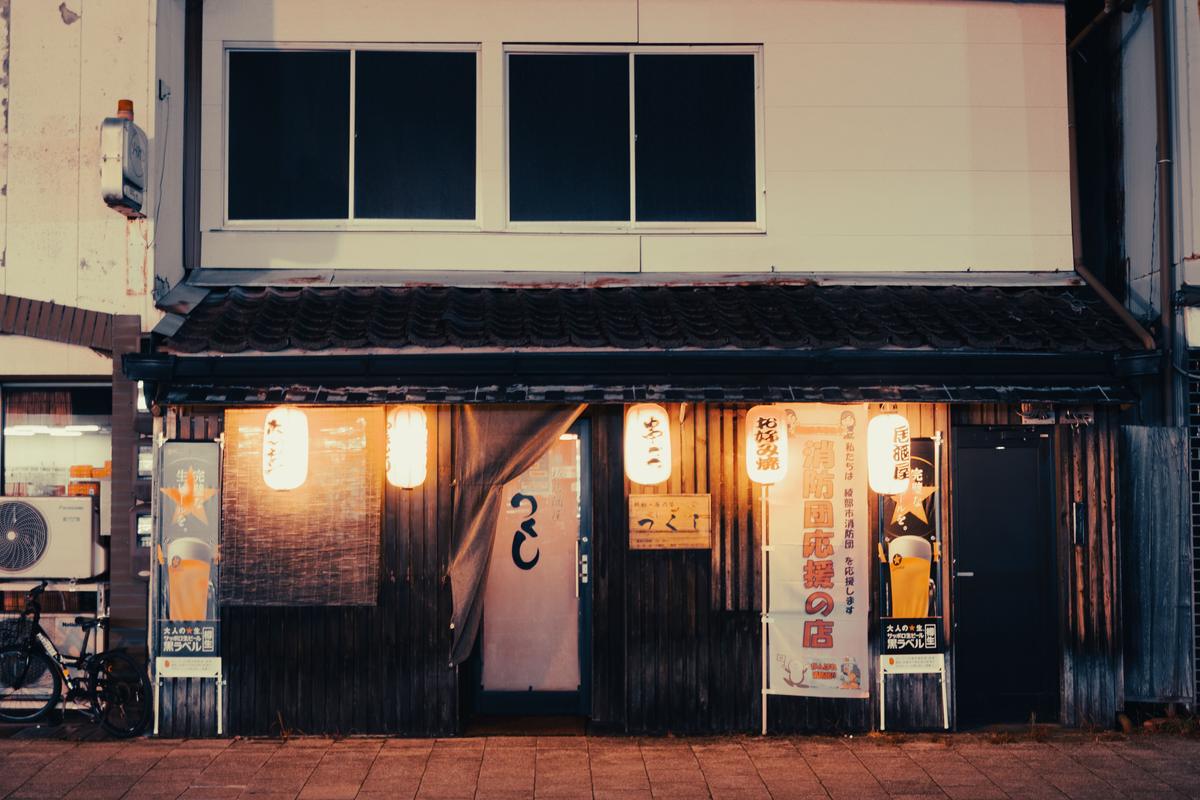 A street corner at night with a Japanese izakaya lit by hanging lanterns