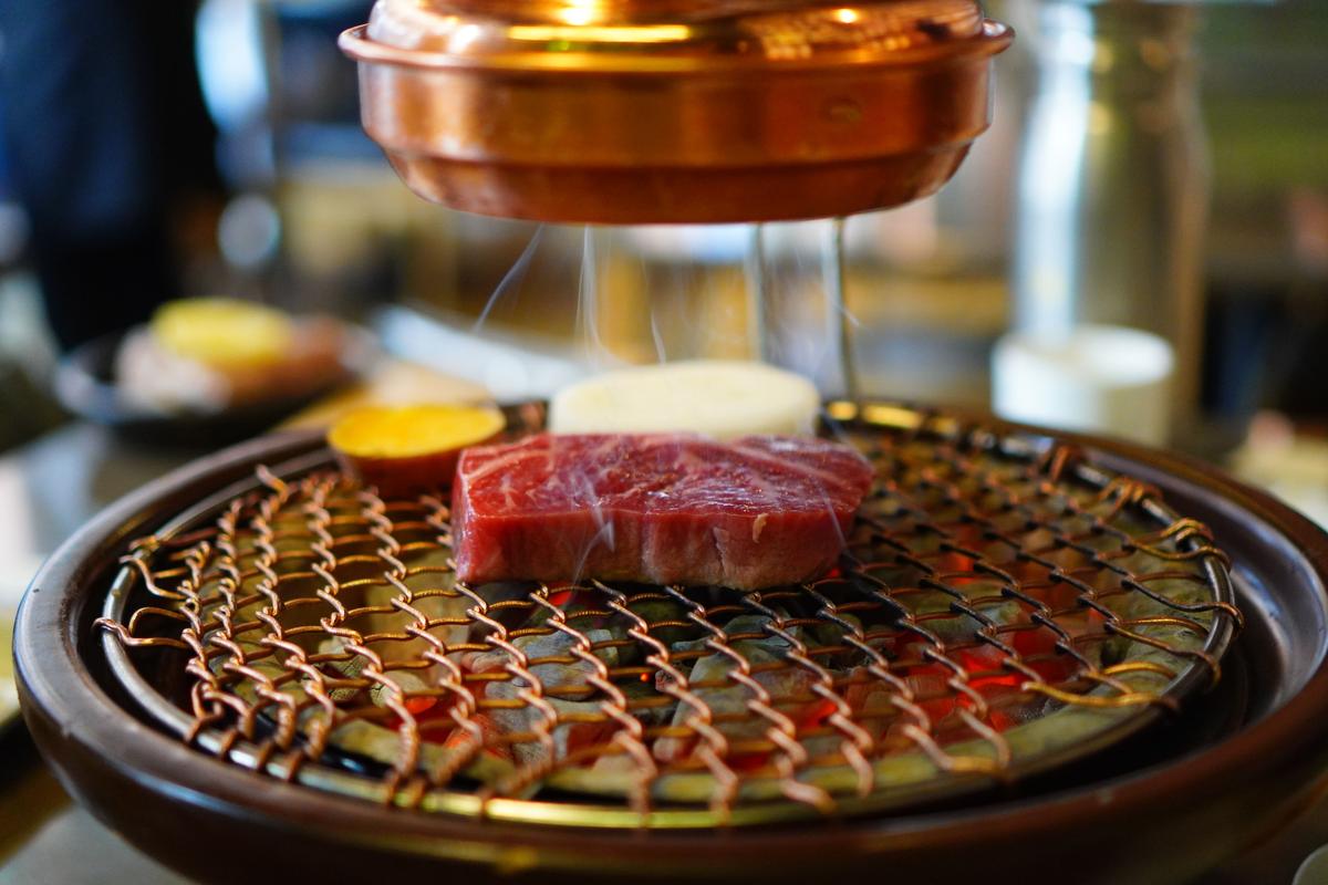 A thick cut of raw marbled beef on a round Korean barbecue grill under a copper hood