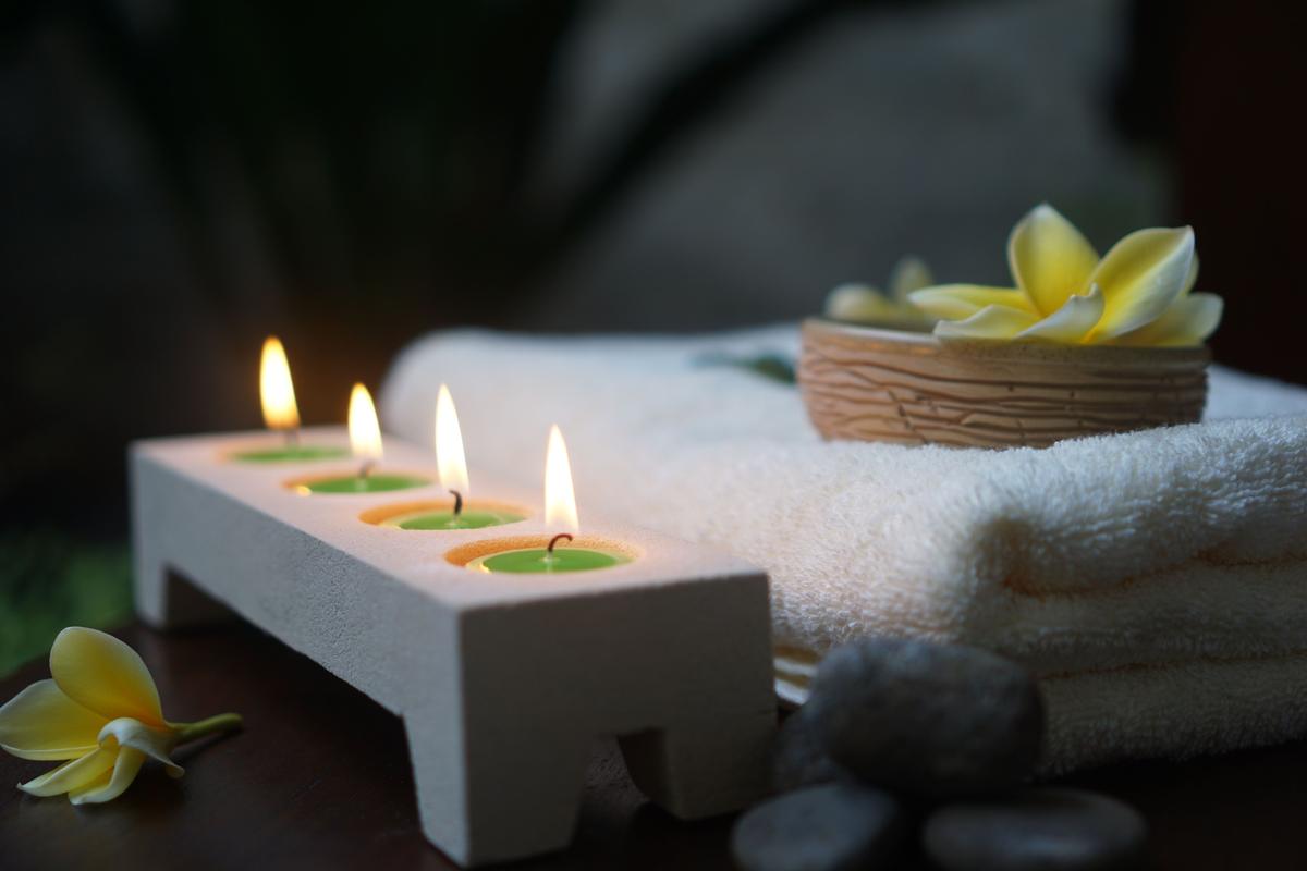 Lit candles, folded white towels, smooth stones and a flower laid out in a spa room
