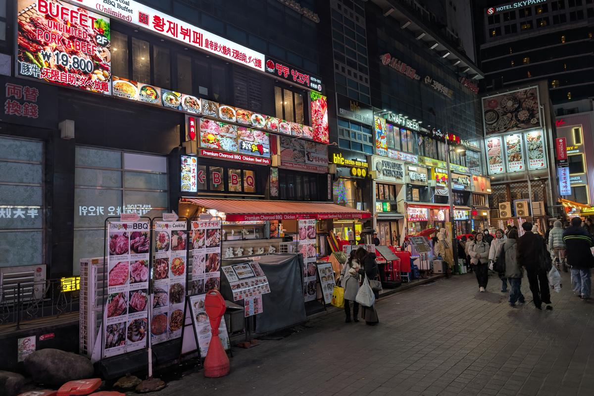 A Seoul street at night lined with lit restaurant signs and menu boards