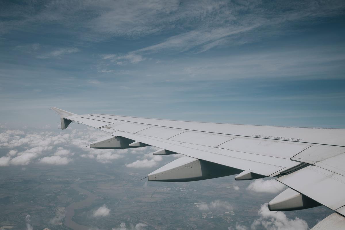 An airplane wing above scattered clouds, seen from a window seat
