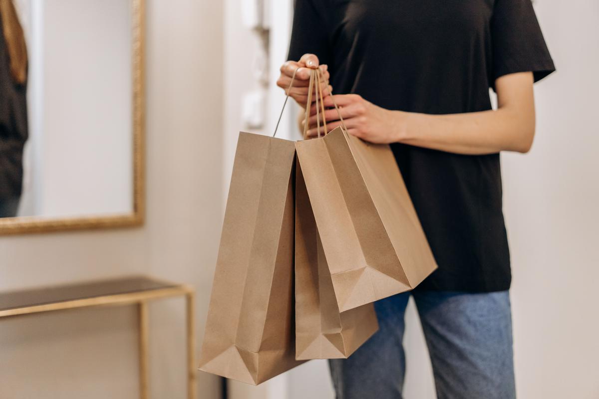 A shopper holding three brown paper shopping bags