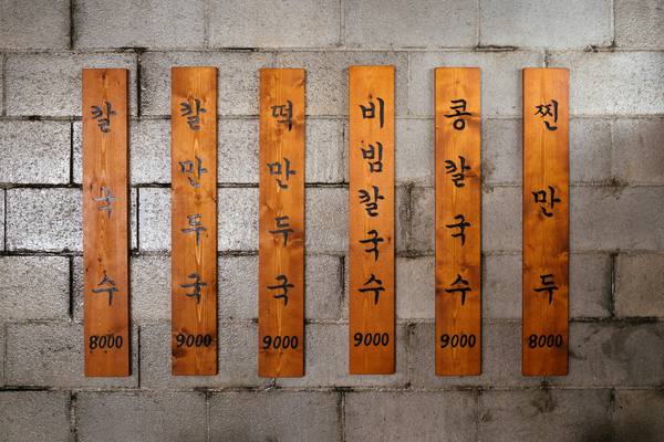 Wooden menu boards written only in Korean, listing noodle and dumpling dishes at 8,000 to 9,000 won