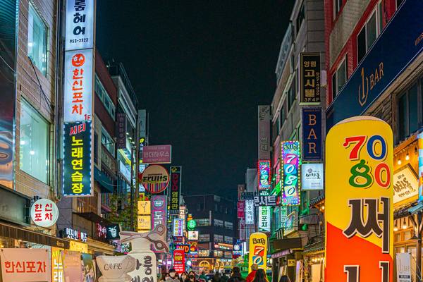 A Seoul street at night crowded with vertical shop signs written in Korean