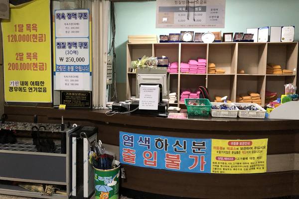 Front desk of a jjimjilbang in Wonju with price signs and a banner saying people with freshly dyed hair may not enter