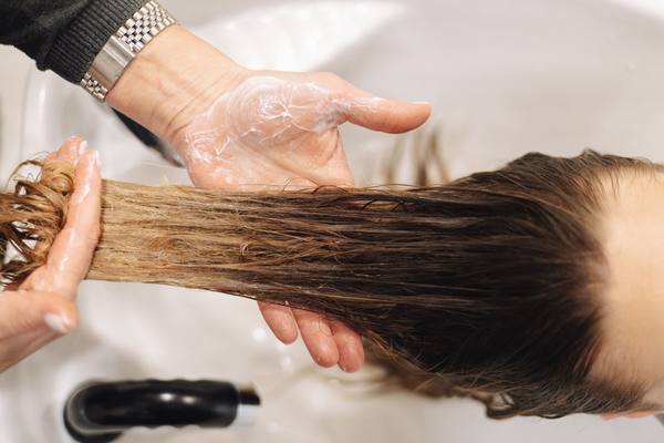 A stylist's hands rinsing long hair over a salon basin