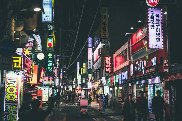 A Seoul street at night lined with lit signs, several of them marked 24시, open 24 hours