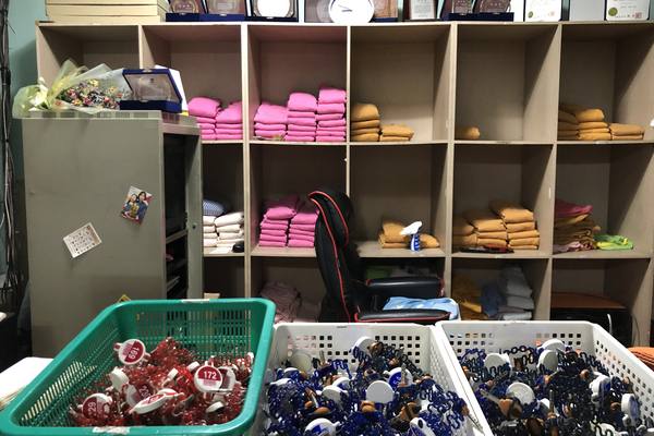 Shelves of folded pink and orange jjimjilbang clothes and towels behind the front desk, with baskets of wristband locker keys in front